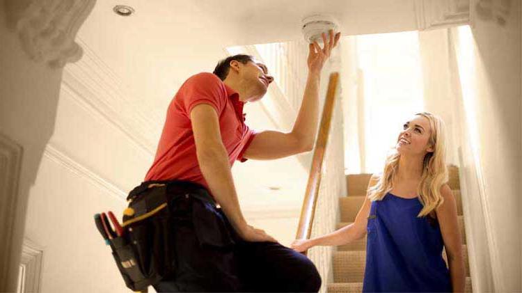 Woman watching man install a smoke detector. 