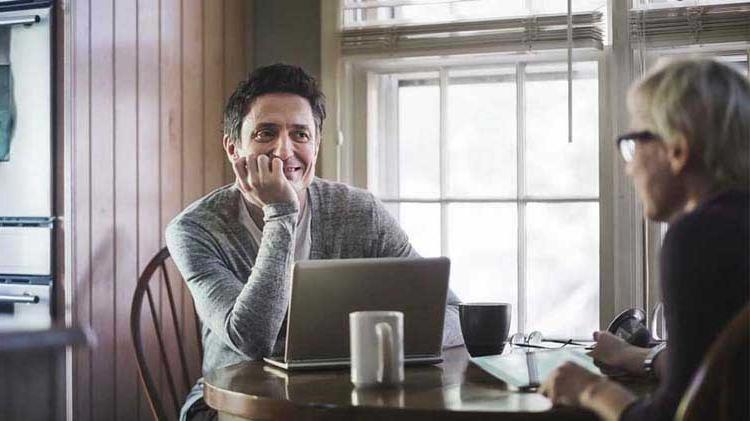 Men conversing in a coffee shop with a laptop.