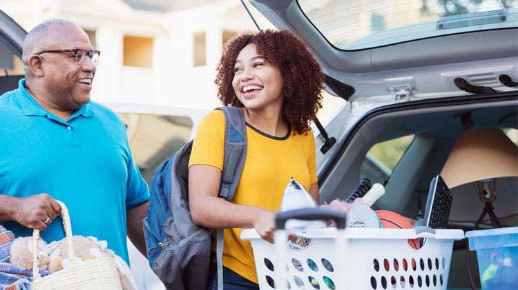 Young woman, preparing for college, loading a laundry basket of items into a car with her father.