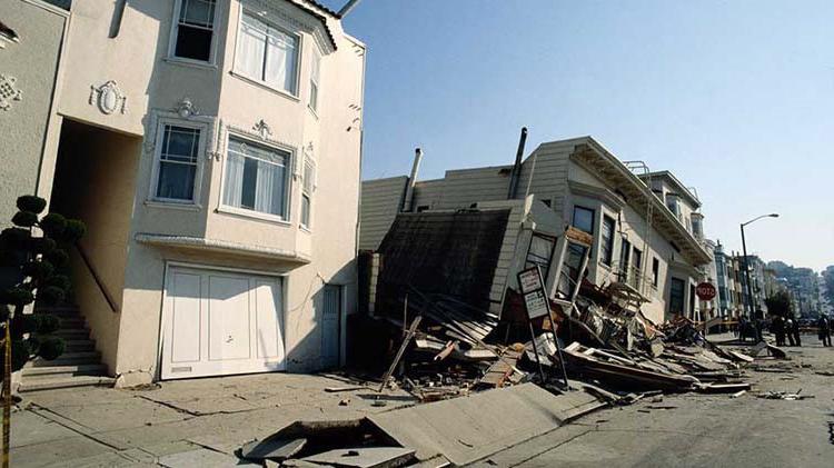 Houses with earthquake damage where one is leaning to the left and sunk in.