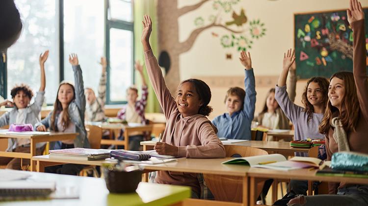 Elementary students raising their hands in class at school.