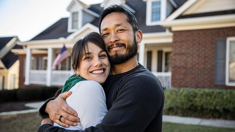 Couple hugging outside their home.