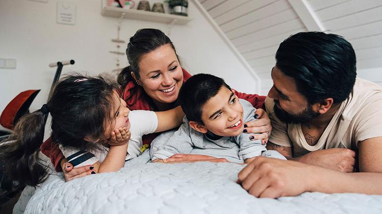 A family with a special needs child is laying on a bed talking and laughing.