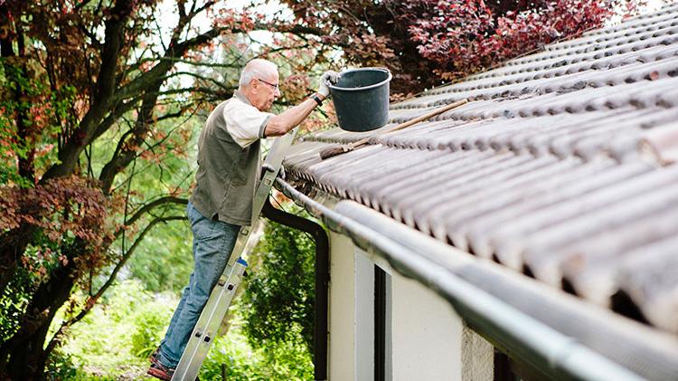 A man cleaning gutters on the roof of a house.