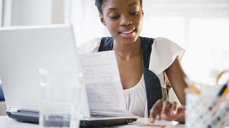 Woman searches through paperwork and on her laptop for a new apartment.