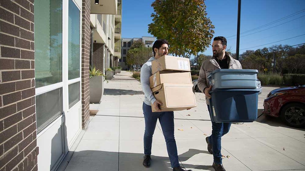 Two men carrying boxes from a building.